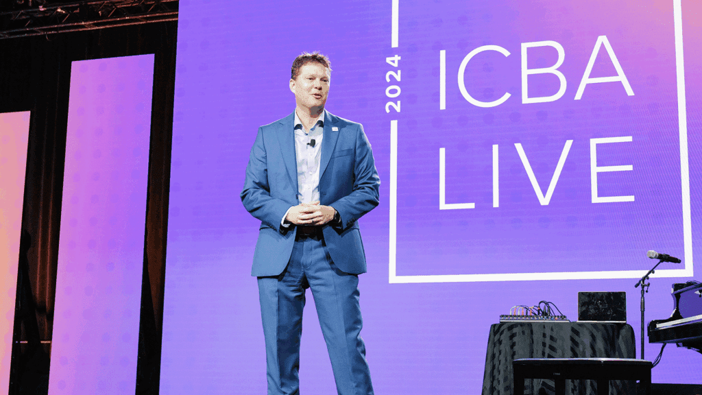 a man standing on a well-lit conference stage delivering an address