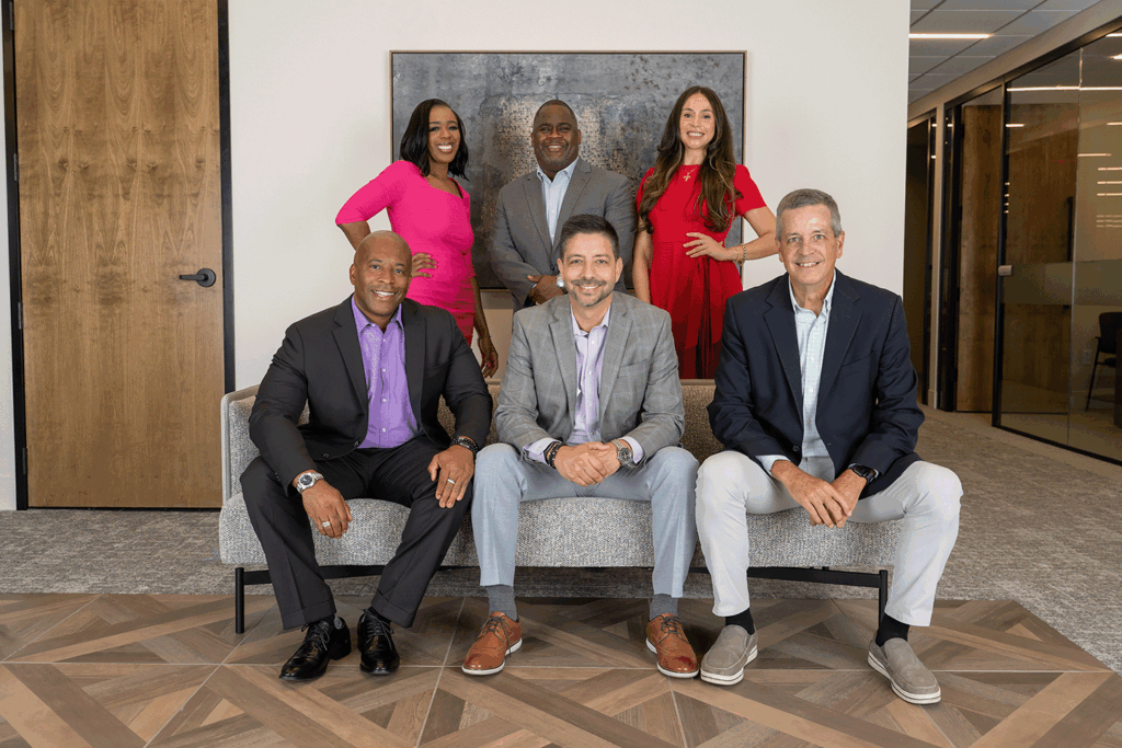 a group photo showing three men sitting on a couch and three more employees standing behind them