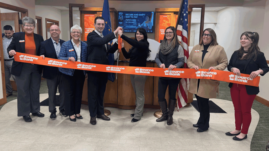 a photo showing eight people in business attire ceremonially cutting a red ribbon inside a bank