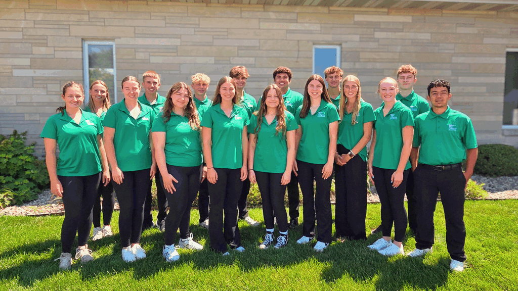 a photo showing the members of Alliance Bank's Junior Board for 2025-26 all wearing black jeans and green polo shirts in front of a limestone building