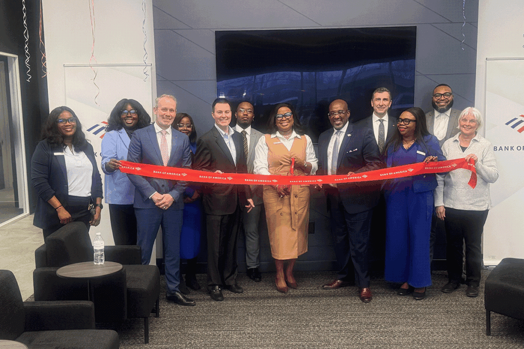 a photo showing a line of 12 people in professional clothing ceremonially cutting a red ribbon inside a commercial building