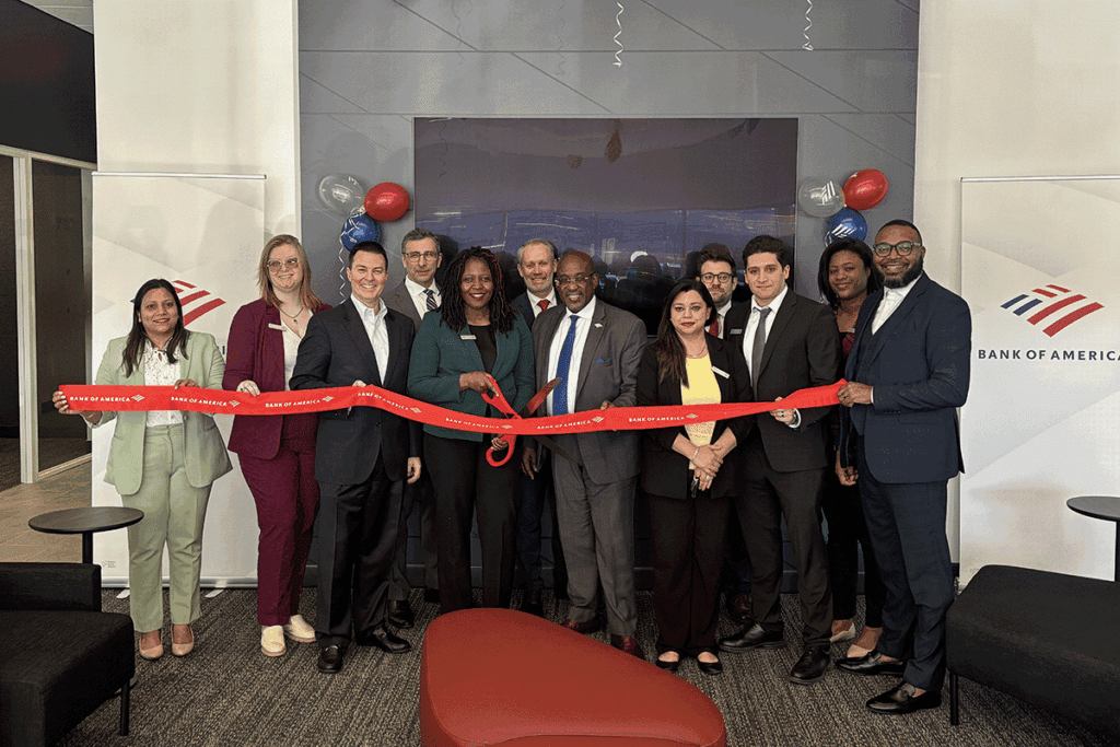 a photo showing a line of 12 people in professional clothing ceremonially cutting a red ribbon inside a commercial building