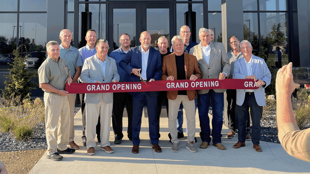 a group of dignitaries cut a ceremonial ribbon in front of a business building