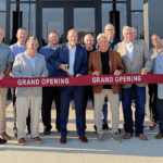 a group of dignitaries cut a ceremonial ribbon in front of a business building