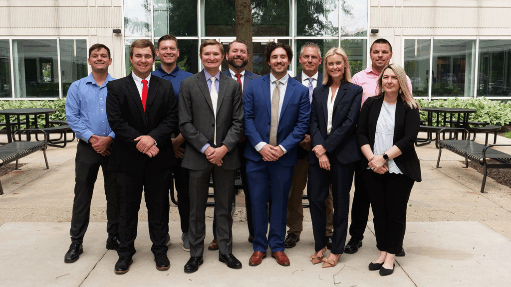 a photo showing 10 bankers in professional clothing standing outside an office building