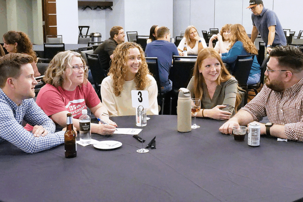 a group of college students sit around a round table inside a conference hall having a discussion