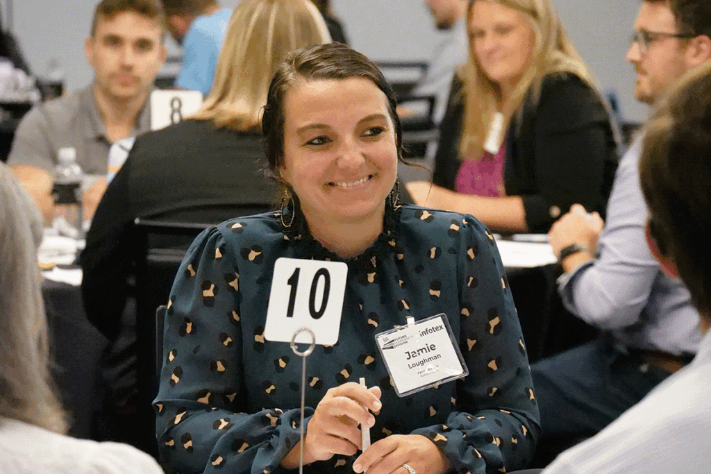 a group of college students and young professionals sit around a round table inside a conference hall having a discussion