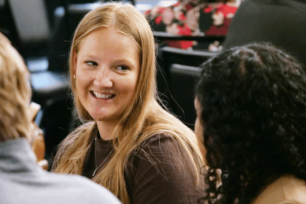 a group of college students and young professionals sit around a round table inside a conference hall having a discussion