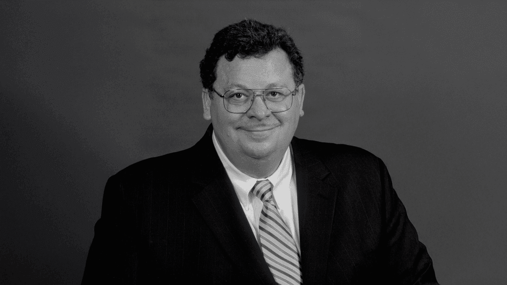 a black & white headshot of a man in a suit and tie