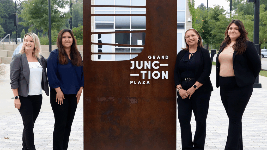 a photo showing four women in professional clothes standing on either side of a sign marking Grand Junction Plaza in Westfield
