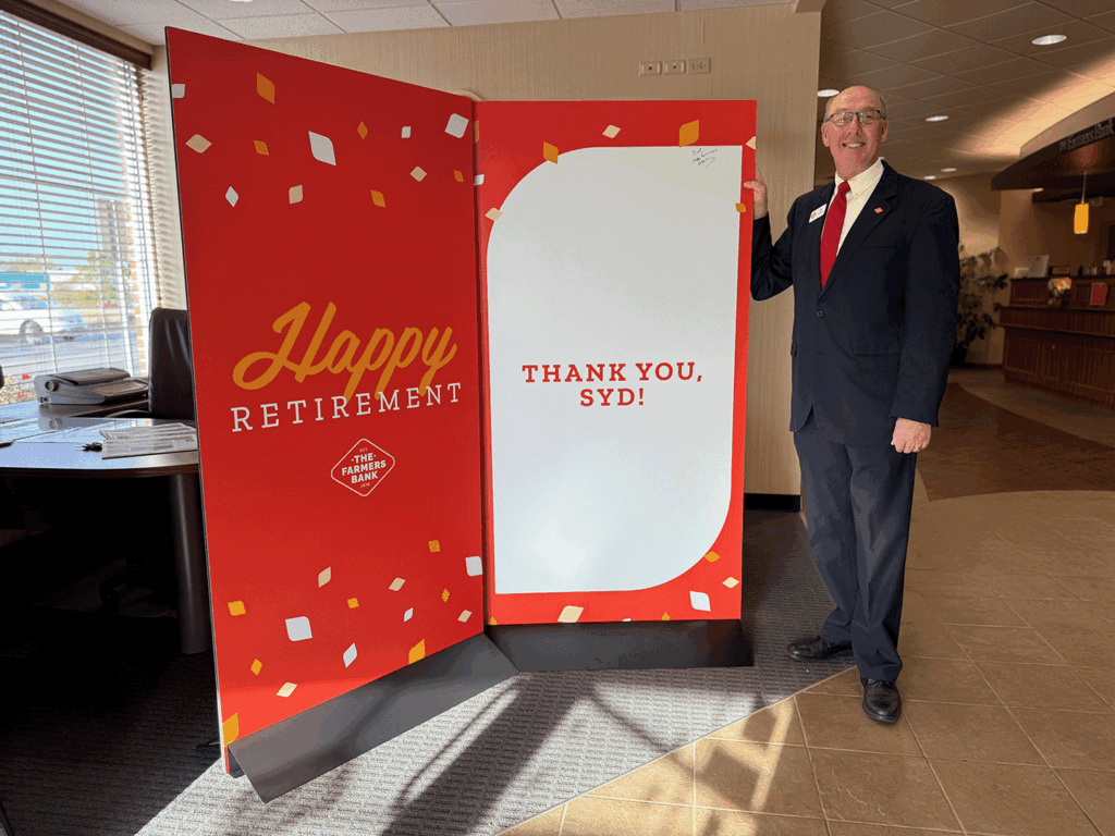 a man in a suit stands next to a card nearly as tall as him congratulating him on his retirement