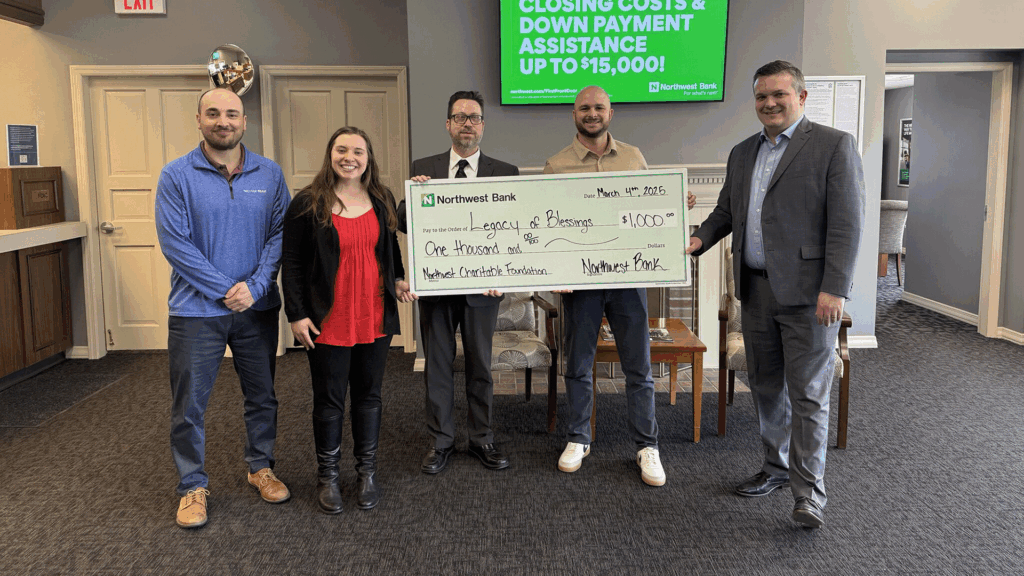 a photo showing five people in professional clothing holding a large ceremonial check inside a bank building representing a charitable donation