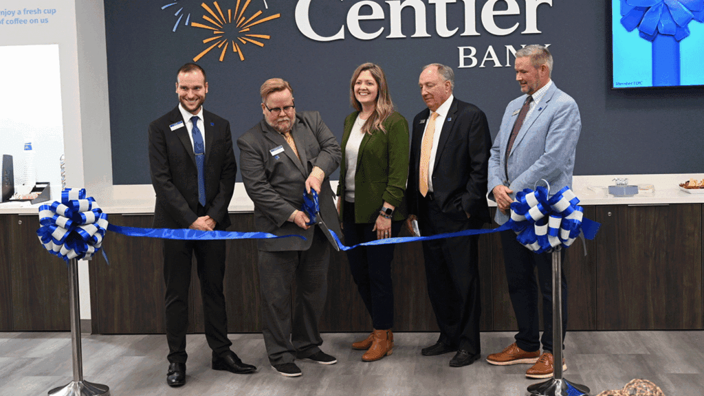 a photo showing five people in professional clothing ceremonially cutting the ribbon inside a new bank branch