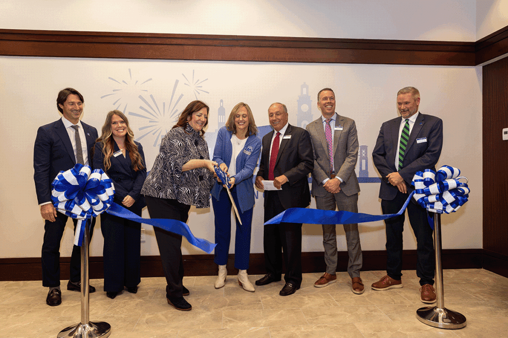 a photo showing seven people in professional clothing ceremonially cutting the ribbon inside a new bank branch
