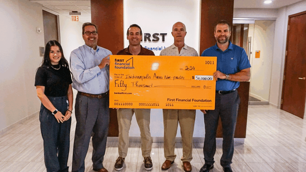 five adults hold a large commemorative check inside a bank building