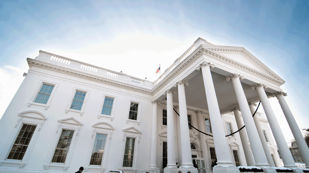 a photo looking up at the portico of the White House from a low angle with a burst of sun shining behind it