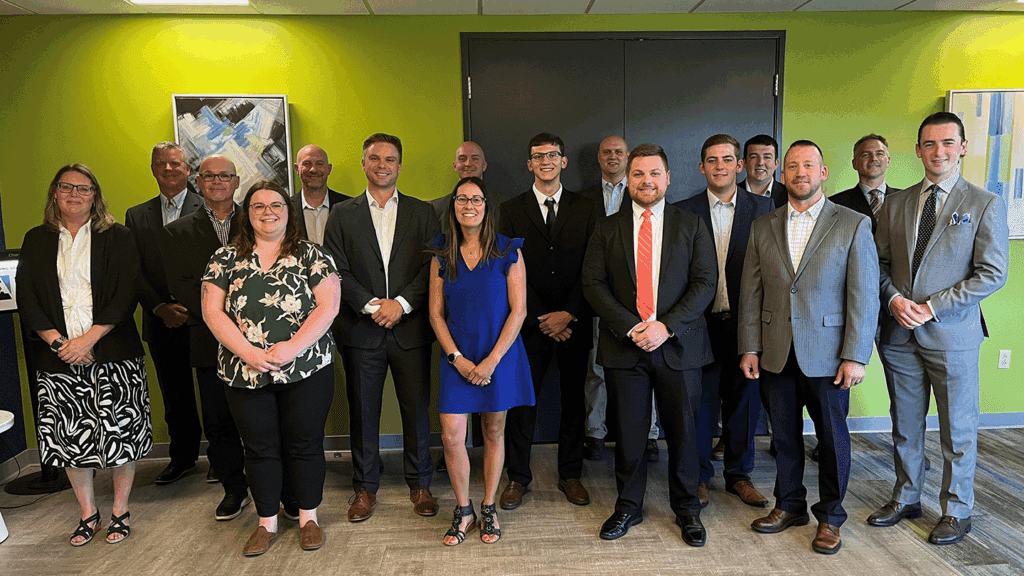 a photo showing 16 people wearing professional clothing posing for a photo inside an office building