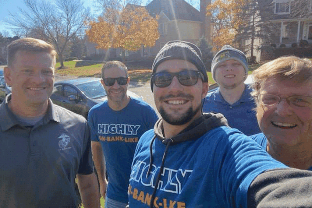 A group of five adults in casual clothing pose for a selfie in the middle of volunteering.