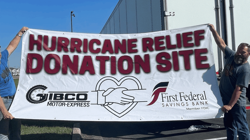 Two volunteers hold a large sign promoting hurricane relief donations.