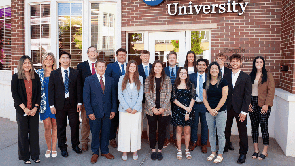 a photo showing 17 college students in professional clothing standing in front of a brick building
