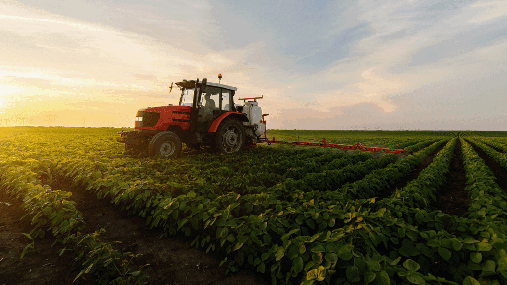 a picture showing a red tractor spraying a soybean field in sunset light