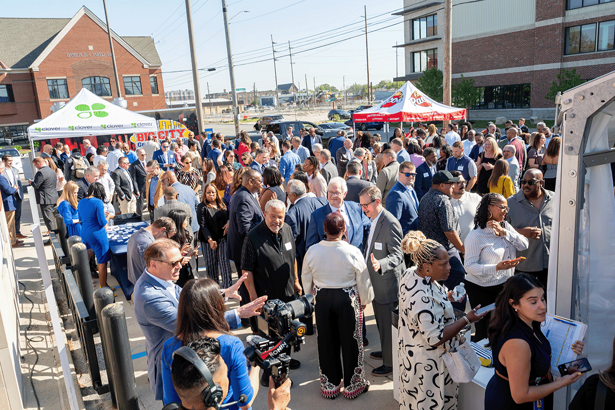 a photo showing a crowd of several hundred attendees gathered in a parking lot ahead of a ceremonial ribbon cutting