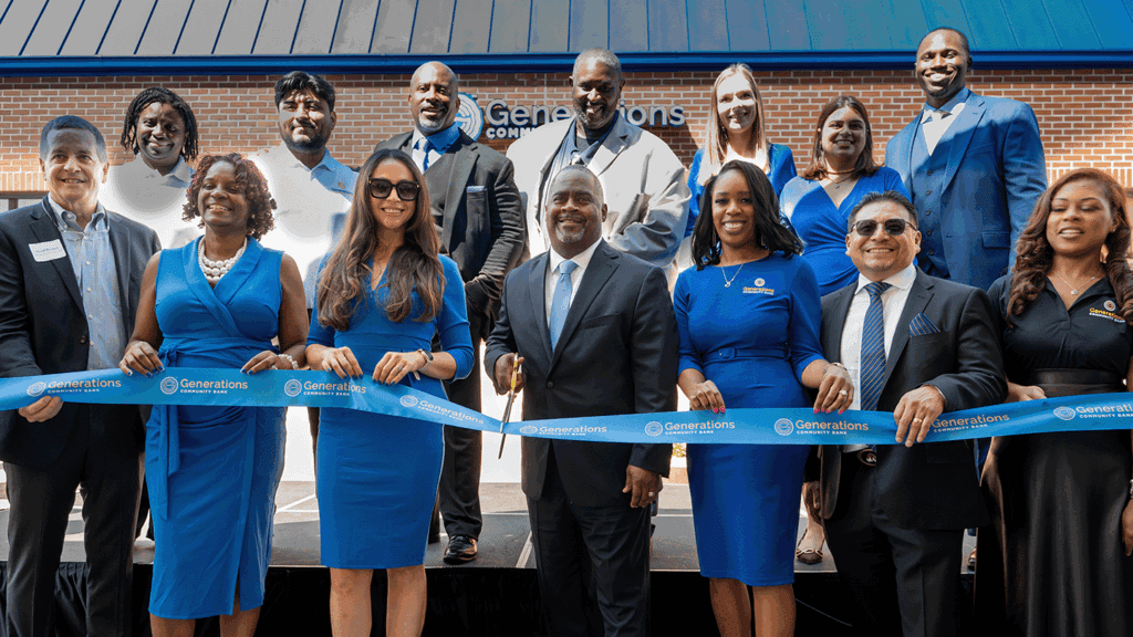A photo showing 14 staff members in blue-themed professional clothing holding a blue ribbon to be cut at the unveiling of a new business, seen behind them