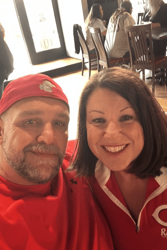 Smiling couple taking a selfie in a cafe; man wears a red cap and red shirt, woman wears a red jacket with white piping.