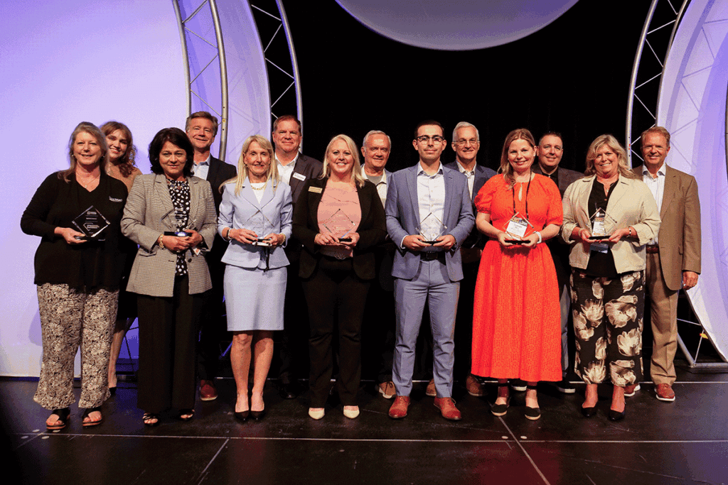Group of professionals on a stage holding glass trophies at an awards ceremony.