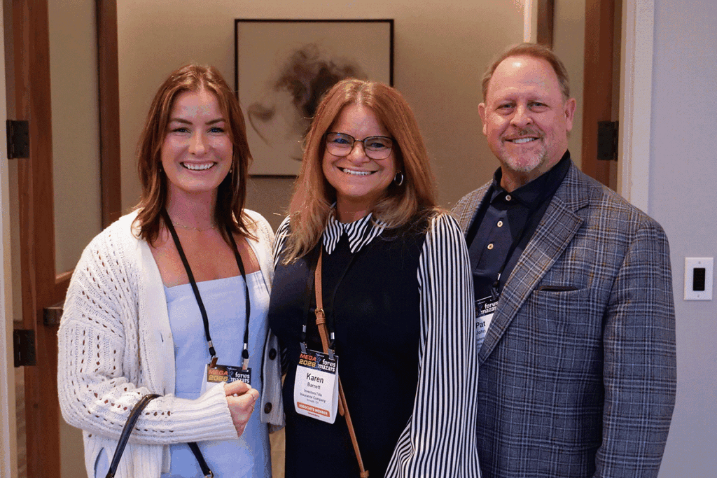 Three smiling colleagues posing for a group photo at a conference, wearing name badges and lanyards.