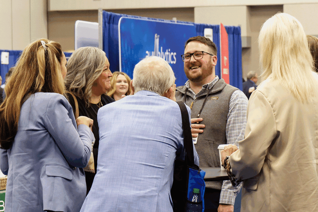 Group of professionals chatting at a trade show booth with a blue backdrop reading 'analytics'.