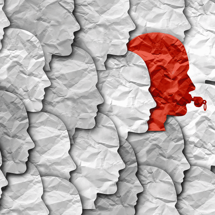 Row of gray paper-cut silhouette profiles facing left; one red figure wearing a headset stands out among them.