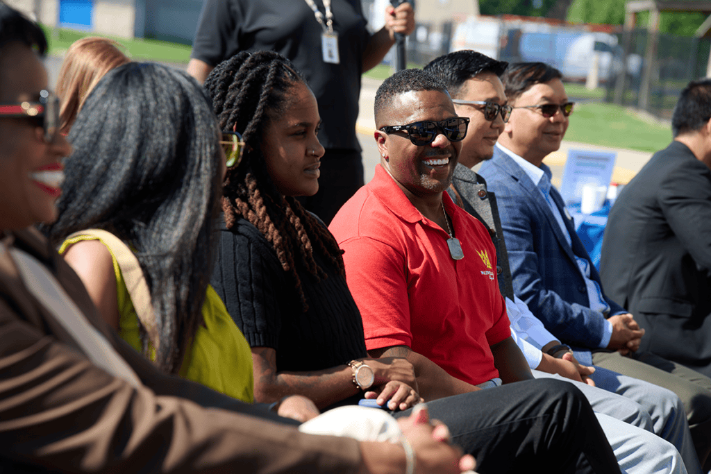 Group of diverse people seated outdoors at an event, smiling and chatting in a row.
