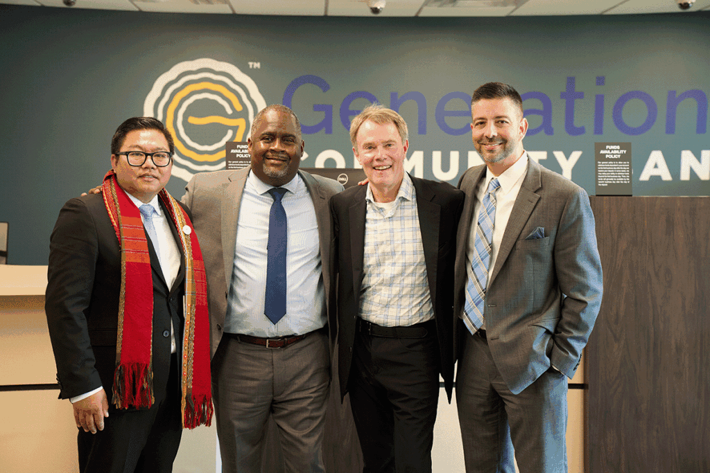 Four men in suits posing together indoors with a 'Generation Community' sign behind them.
