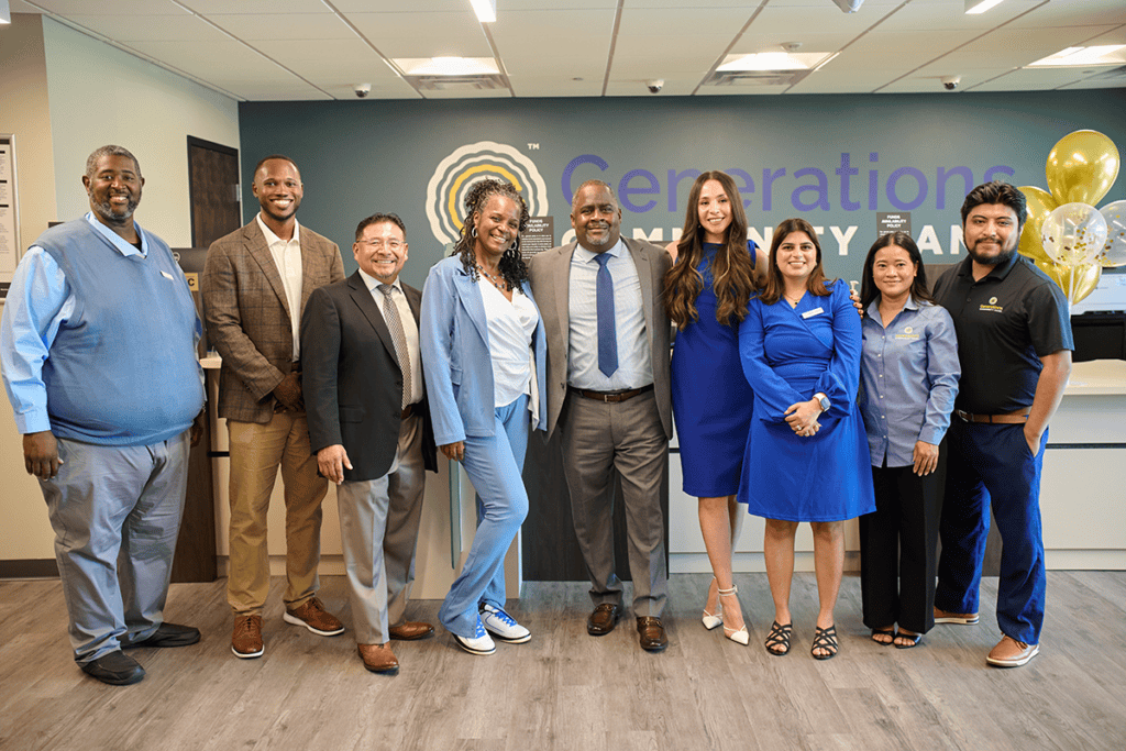 Diverse group of ten professionals posing together in an office lobby with a blue wall and a Generations sign behind them.