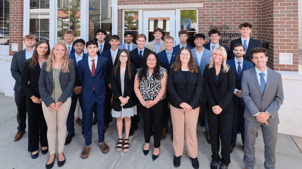 Twenty-two college students in professional clothing pose for a photo in front of a brick building.