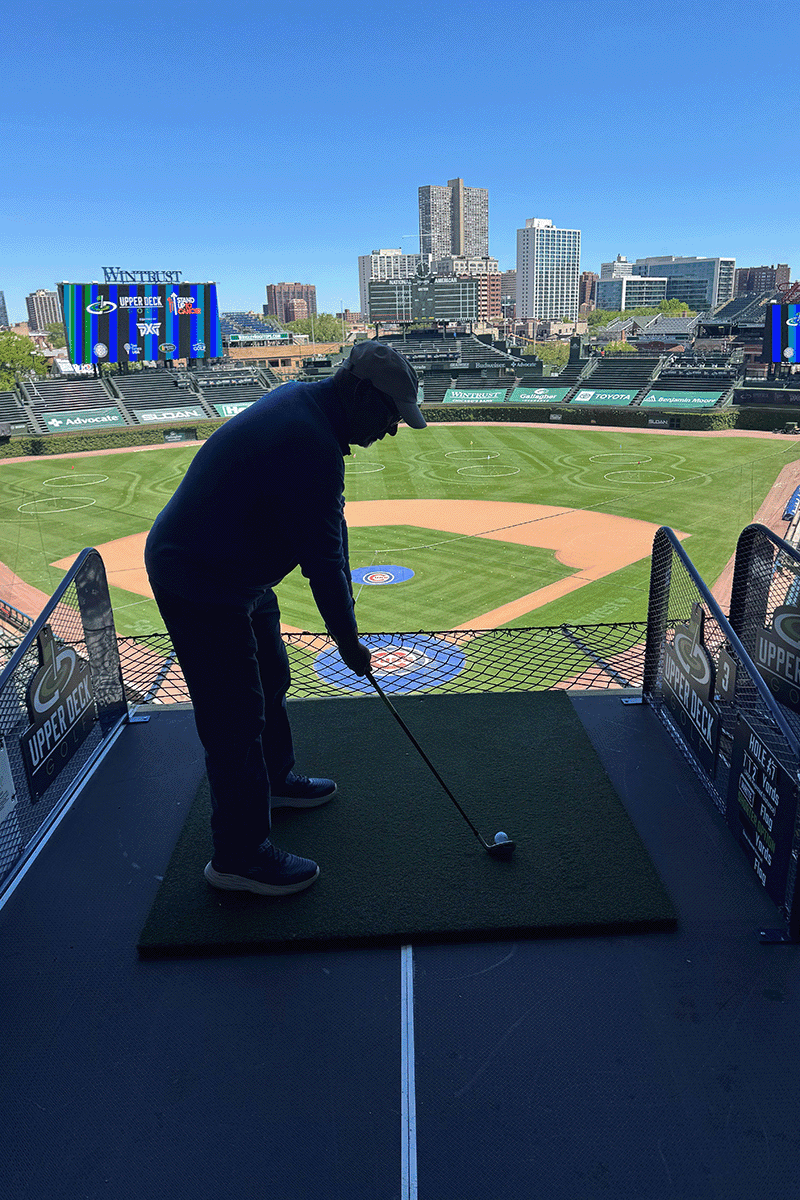 A man tees up a golf shot into a baseball stadium